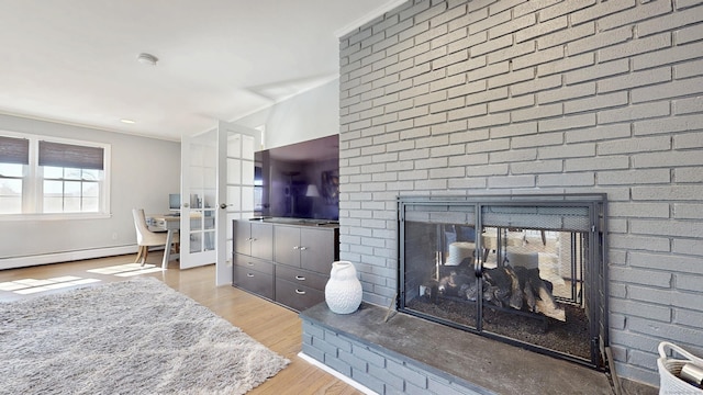 living area featuring baseboard heating, a brick fireplace, and wood finished floors