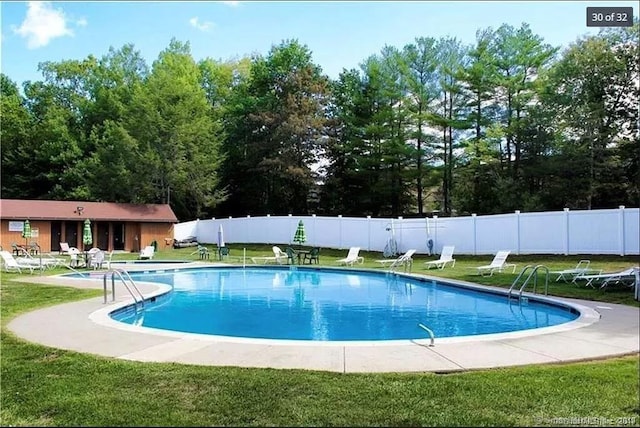 community pool with a patio area, a lawn, and fence