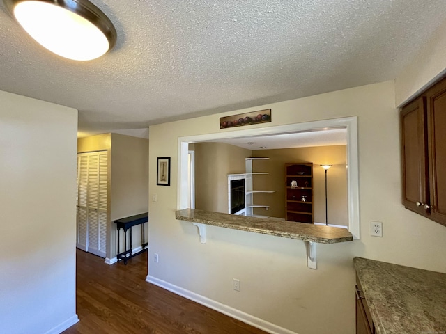 kitchen featuring baseboards, brown cabinets, a fireplace, dark wood-style floors, and a textured ceiling