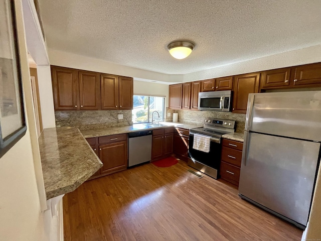 kitchen featuring wood finished floors, a sink, light countertops, appliances with stainless steel finishes, and backsplash