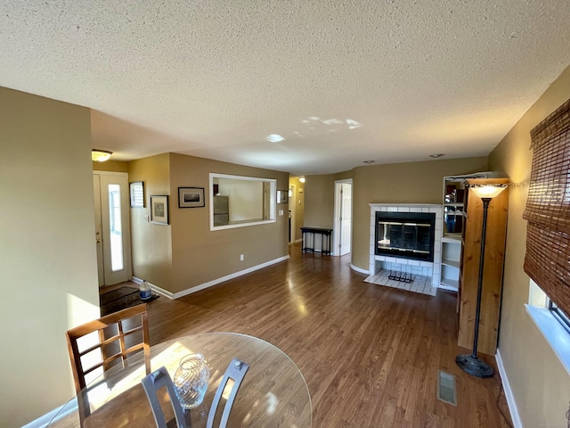 living room featuring wood finished floors, baseboards, visible vents, a textured ceiling, and a tiled fireplace