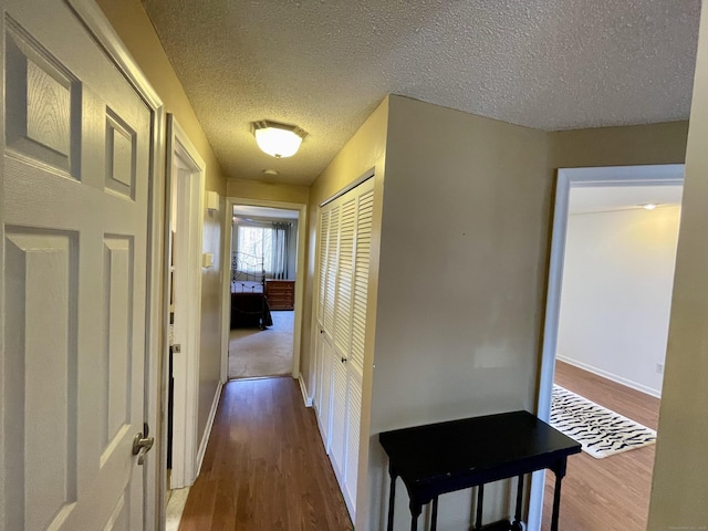 corridor with baseboards, a textured ceiling, and wood finished floors