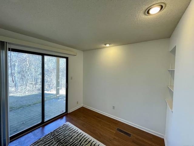 unfurnished room with dark wood-style floors, visible vents, a textured ceiling, and baseboards