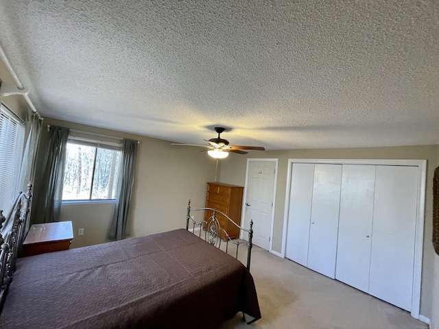 bedroom featuring a textured ceiling, light colored carpet, a closet, and ceiling fan