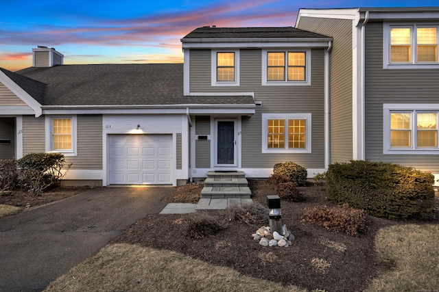 multi unit property featuring a garage, roof with shingles, a chimney, and aphalt driveway