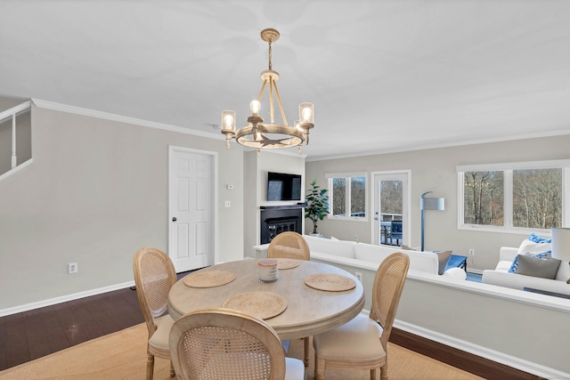 dining space featuring ornamental molding, wood finished floors, an inviting chandelier, a fireplace, and baseboards