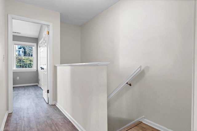 hall featuring an upstairs landing, baseboards, and wood finished floors