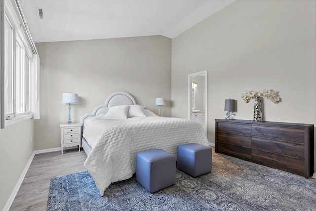 bedroom featuring visible vents, lofted ceiling, ensuite bath, wood finished floors, and baseboards