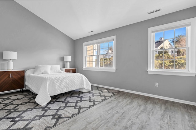 bedroom featuring lofted ceiling, visible vents, baseboards, and wood finished floors