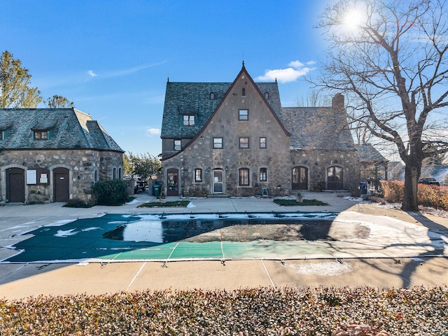 exterior space with a high end roof, stone siding, and a chimney