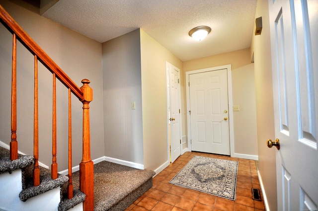 tiled entrance foyer featuring visible vents, baseboards, a textured ceiling, and stairway