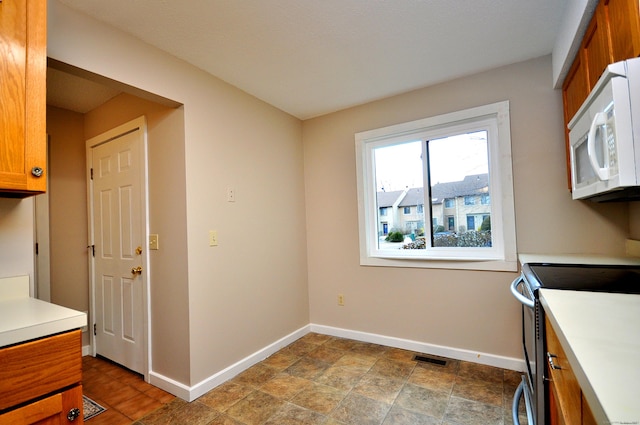 kitchen with visible vents, brown cabinets, stainless steel range with electric stovetop, baseboards, and white microwave