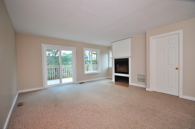 unfurnished living room featuring visible vents, baseboards, a fireplace with flush hearth, carpet flooring, and a textured ceiling