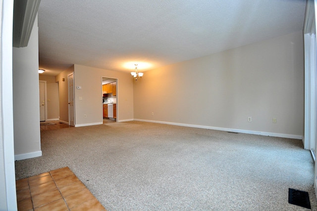 spare room with visible vents, baseboards, a textured ceiling, light carpet, and a chandelier