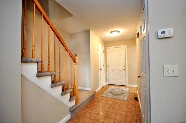 foyer entrance with light tile patterned floors, stairway, baseboards, and a textured ceiling