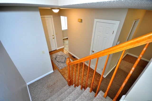 staircase with carpet flooring, baseboards, and a textured ceiling