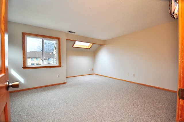 empty room featuring a skylight, carpet flooring, baseboards, and visible vents