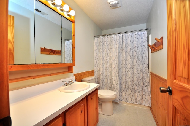 bathroom with toilet, visible vents, a wainscoted wall, and a textured ceiling