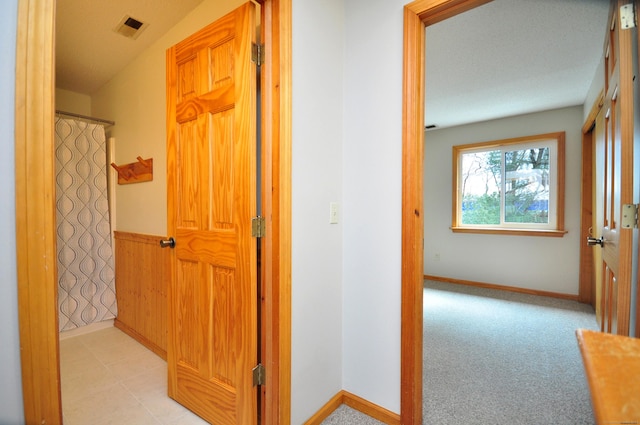 corridor featuring light carpet, baseboards, visible vents, and wainscoting