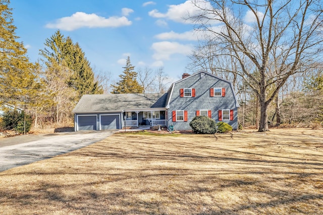 view of front of house featuring a gambrel roof, driveway, covered porch, an attached garage, and a chimney