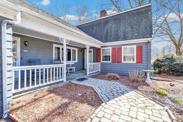 property entrance with a chimney, a porch, and a shingled roof