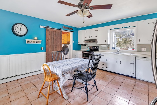 dining space with a wainscoted wall, a ceiling fan, a barn door, light tile patterned flooring, and washer / dryer