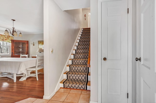 stairway featuring an inviting chandelier, tile patterned floors, crown molding, and baseboards