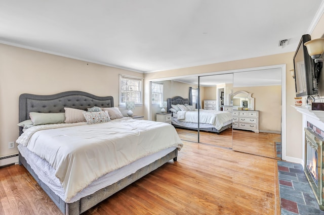 bedroom with visible vents, wood finished floors, a fireplace, crown molding, and baseboards