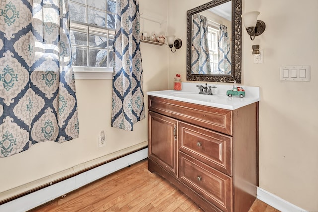 bathroom with a wealth of natural light, baseboard heating, vanity, and wood finished floors