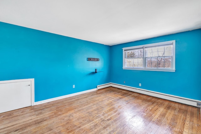 empty room featuring a baseboard heating unit, baseboards, and wood finished floors