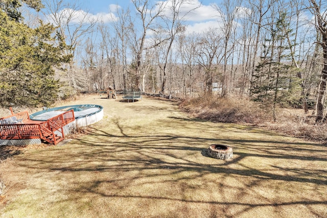 view of yard with a wooden deck, a fire pit, and a trampoline