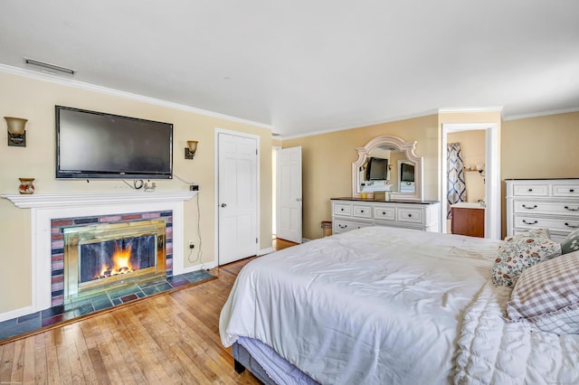 bedroom featuring visible vents, ornamental molding, a glass covered fireplace, hardwood / wood-style floors, and baseboards