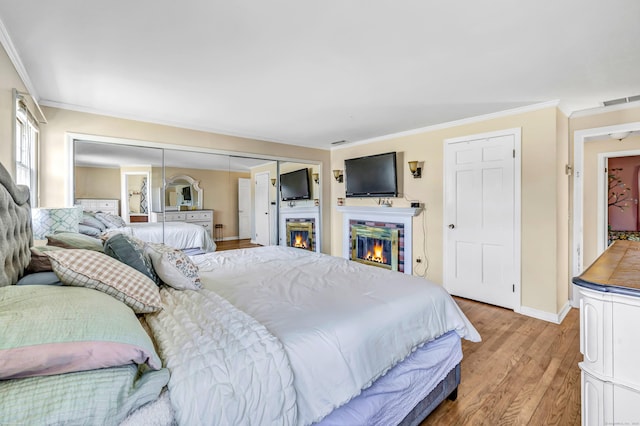 bedroom featuring baseboards, visible vents, a glass covered fireplace, crown molding, and light wood-type flooring