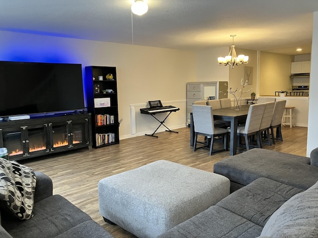 living area featuring a notable chandelier, a glass covered fireplace, a textured ceiling, and wood finished floors