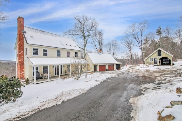 snow covered rear of property with a detached garage, a chimney, and dirt driveway