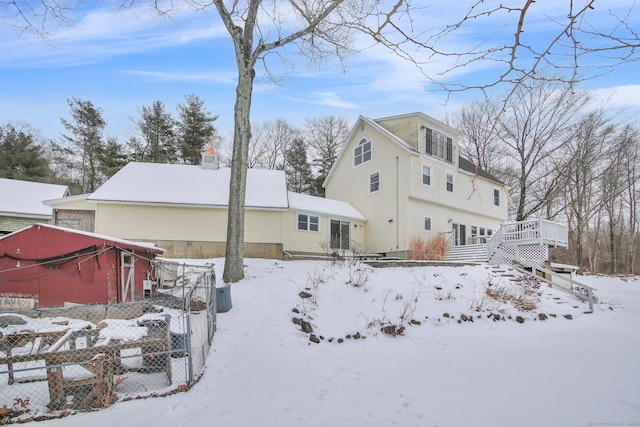 snow covered property with a deck, fence, and a garage