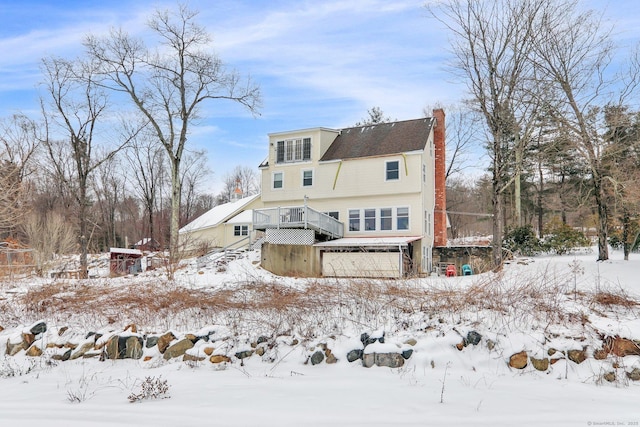 snow covered house featuring a wooden deck, a garage, and a chimney