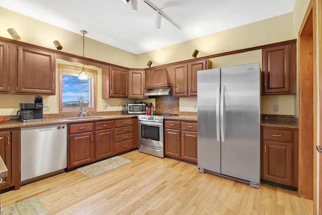 kitchen with decorative light fixtures, light wood-type flooring, appliances with stainless steel finishes, brown cabinetry, and a sink