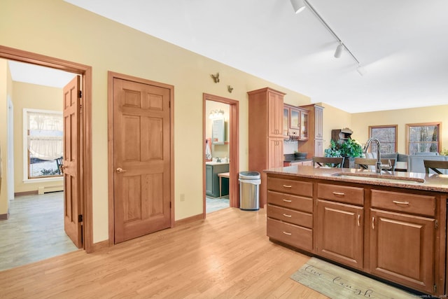 kitchen featuring a baseboard heating unit, glass insert cabinets, light wood-style flooring, brown cabinets, and a sink