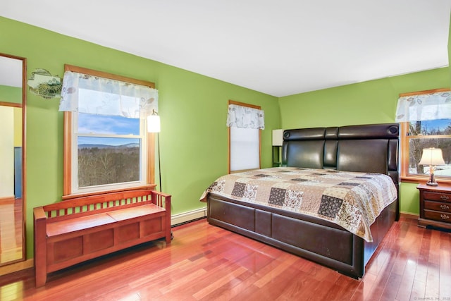 bedroom featuring a baseboard heating unit, wood finished floors, and baseboards