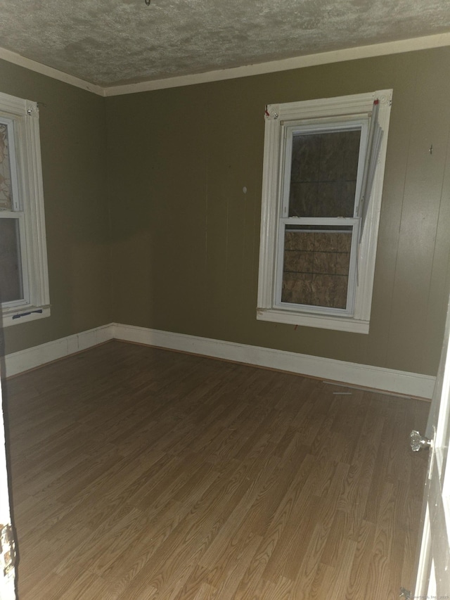 spare room featuring baseboards, a textured ceiling, wood finished floors, and crown molding