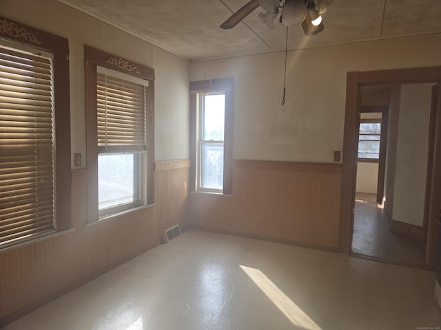 empty room with visible vents, a ceiling fan, and wainscoting