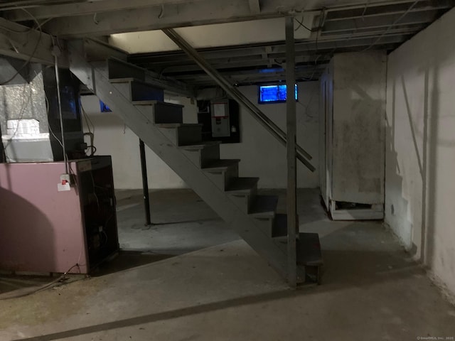 unfinished below grade area featuring electric panel, stairway, and heating unit