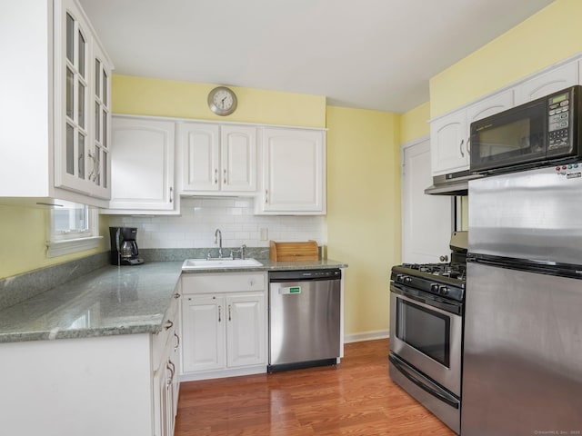 kitchen with glass insert cabinets, under cabinet range hood, white cabinets, stainless steel appliances, and a sink