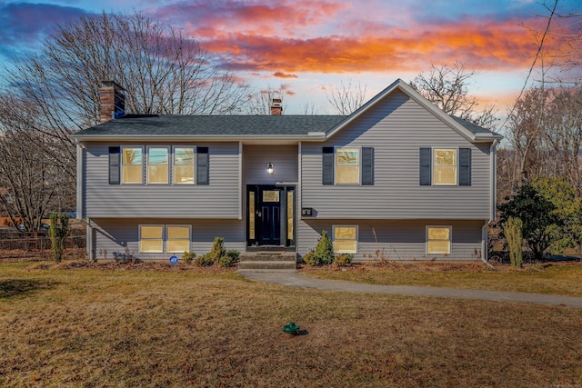 raised ranch featuring a shingled roof, a front yard, and a chimney