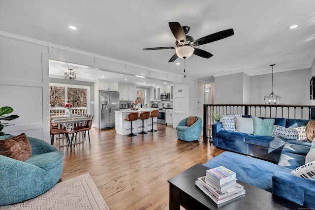 living room featuring recessed lighting, light wood-style floors, crown molding, and ceiling fan with notable chandelier