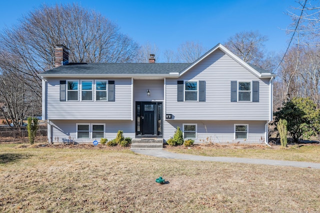 raised ranch featuring a chimney, a front lawn, and a shingled roof