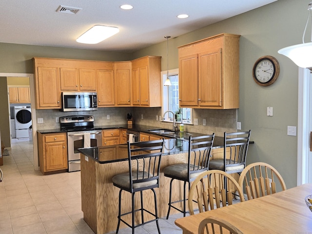 kitchen featuring visible vents, a sink, appliances with stainless steel finishes, a peninsula, and washer / dryer