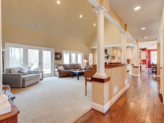 living room with decorative columns, visible vents, wood-type flooring, and high vaulted ceiling