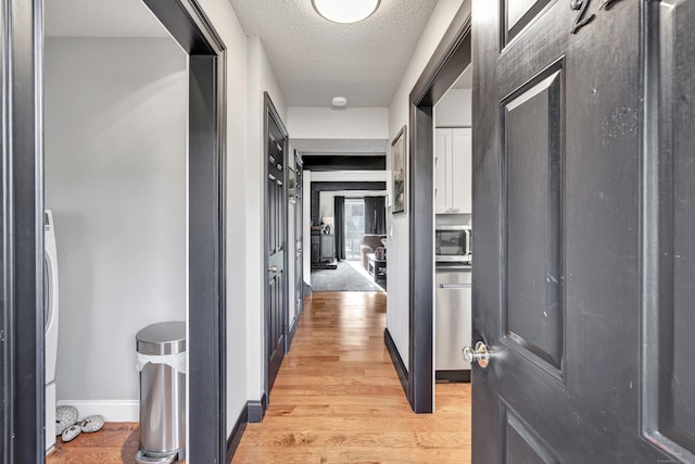 corridor featuring light wood-style floors, baseboards, and a textured ceiling